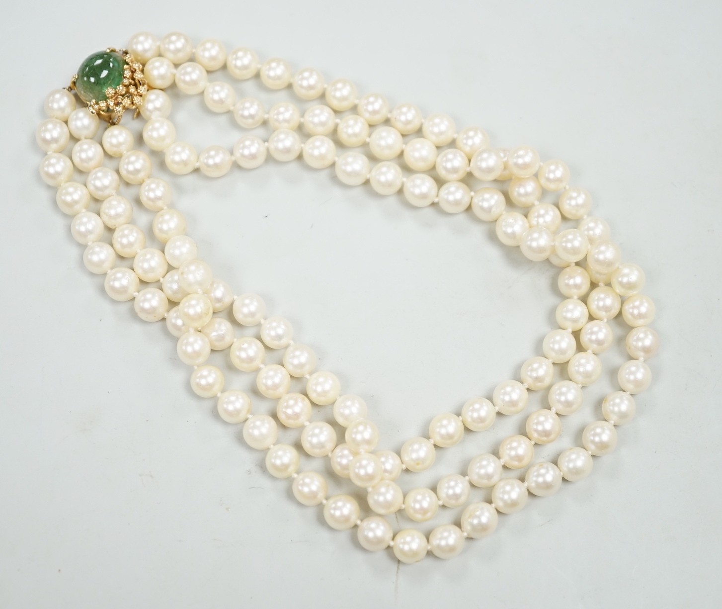 A mid to late 29th century triple strand cultured pearl choker necklace, with 14k and cabochon emerald set clasp, 34cm.